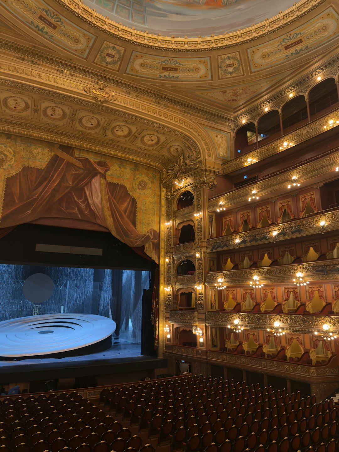 Teatro vuoto e ornato con balconate a più livelli e un palco moderno.