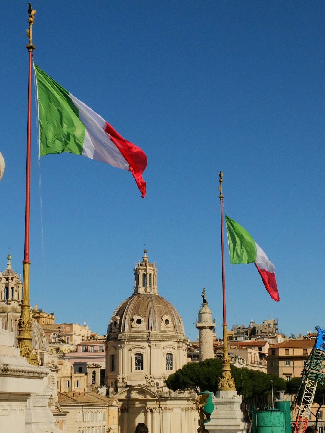 Due bandiere italiane sventolano da aste dorate ornate contro il cielo blu.