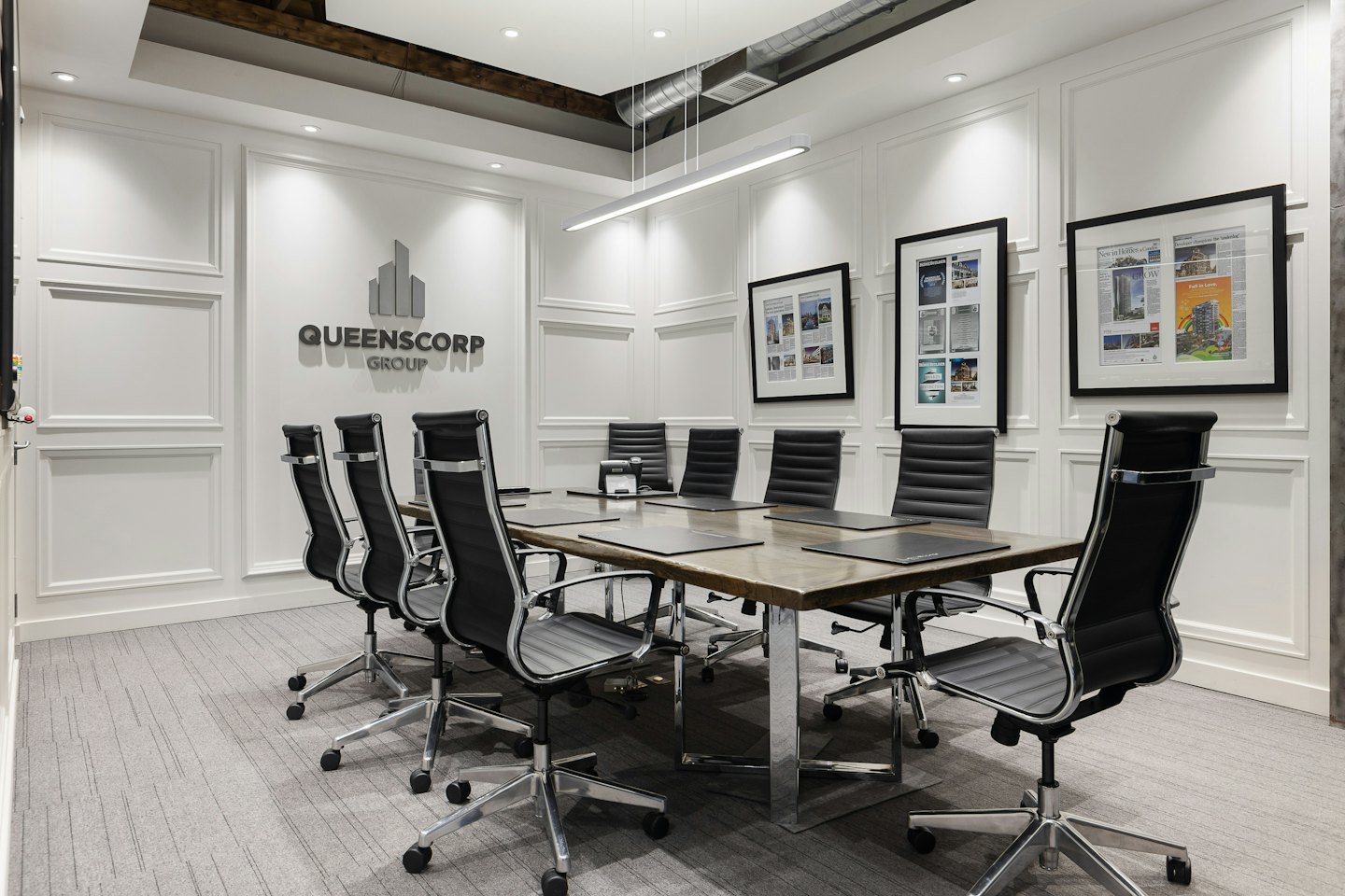 Sala riunioni con lungo tavolo e logo Queenscorp Group.